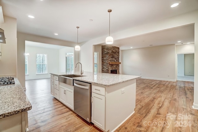 kitchen featuring decorative light fixtures, a center island with sink, appliances with stainless steel finishes, white cabinets, and light stone counters