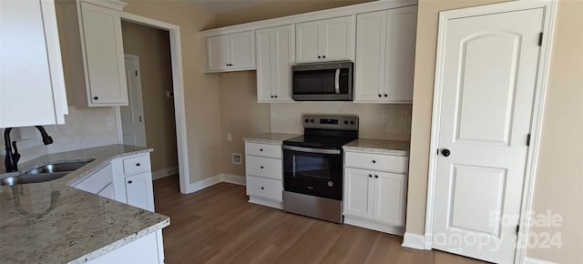 kitchen with backsplash, sink, white cabinetry, appliances with stainless steel finishes, and light stone counters