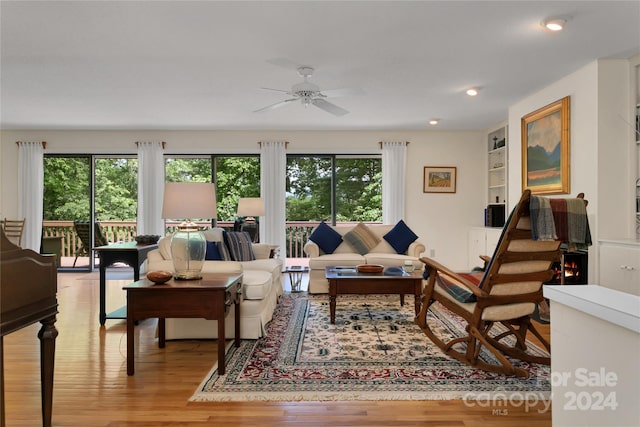 living room featuring ceiling fan, built in features, plenty of natural light, and light hardwood / wood-style flooring