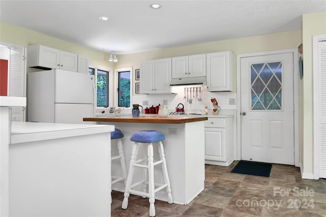 kitchen with white cabinets, wooden counters, white fridge, tasteful backsplash, and a kitchen breakfast bar