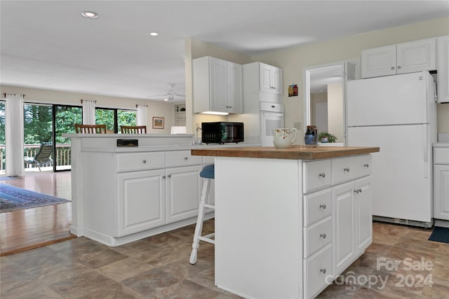 kitchen featuring white cabinetry, a kitchen bar, kitchen peninsula, white appliances, and a center island