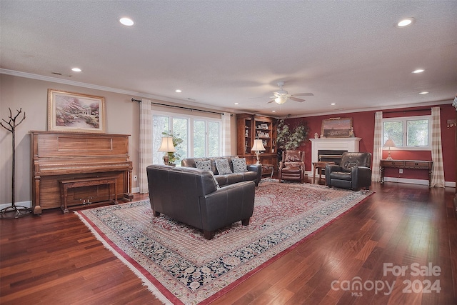 living room with ceiling fan, ornamental molding, dark wood-type flooring, and a textured ceiling