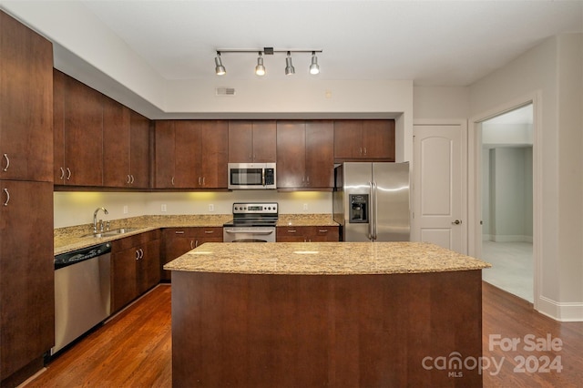 kitchen with appliances with stainless steel finishes, dark hardwood / wood-style flooring, dark brown cabinetry, sink, and a center island