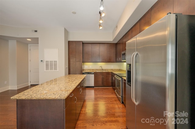 kitchen with sink, stainless steel appliances, light stone counters, dark hardwood / wood-style floors, and a kitchen island