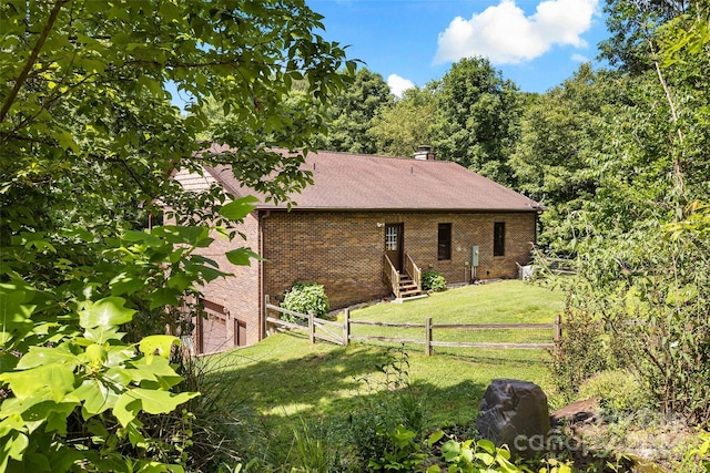 back of house featuring entry steps, a garage, brick siding, fence, and a lawn