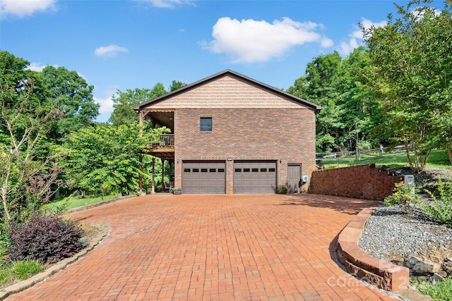 view of property exterior with a garage, brick siding, decorative driveway, and a balcony