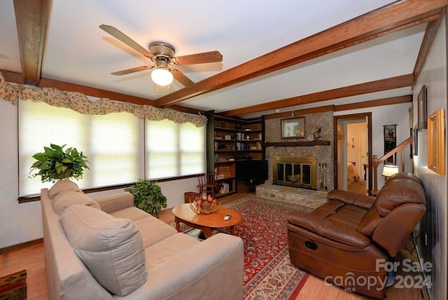 living room featuring hardwood / wood-style flooring, a stone fireplace, ceiling fan, beam ceiling, and built in shelves