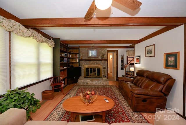 living room with a stone fireplace, beamed ceiling, light hardwood / wood-style floors, built in features, and ceiling fan