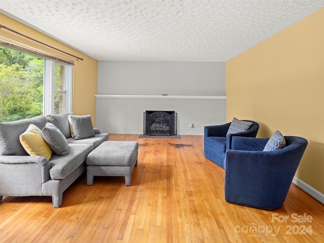 living room featuring hardwood / wood-style flooring, brick wall, a fireplace, and a textured ceiling