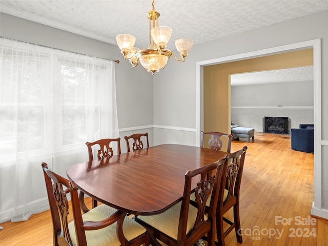 dining room featuring a brick fireplace, a textured ceiling, a chandelier, and light wood-type flooring