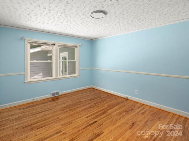 empty room with wood-type flooring, a textured ceiling, and crown molding