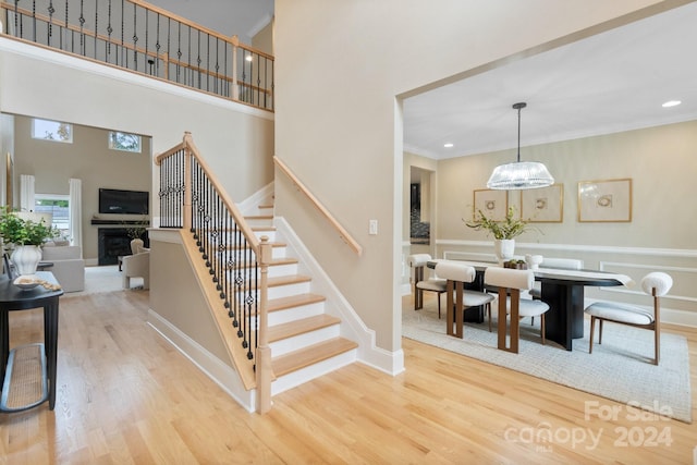 stairs with a towering ceiling, wood-type flooring, a notable chandelier, and ornamental molding