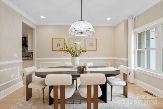 dining room featuring plenty of natural light, light wood-type flooring, ornamental molding, and an inviting chandelier