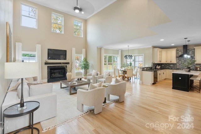 living room featuring sink, a towering ceiling, light hardwood / wood-style floors, and ornamental molding