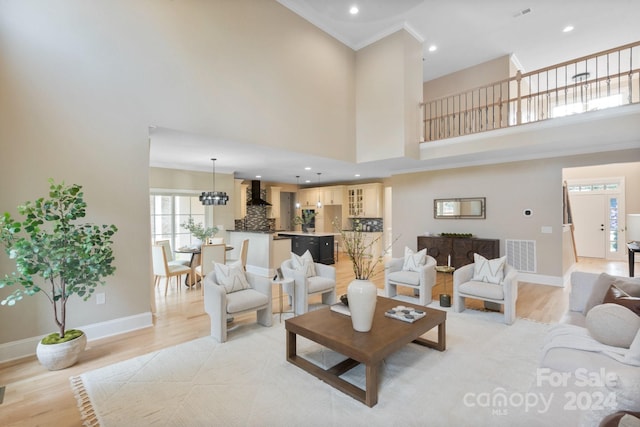 living room with light wood-type flooring, crown molding, a high ceiling, and an inviting chandelier