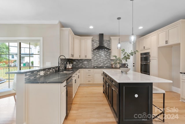 kitchen featuring a center island, sink, wall chimney exhaust hood, pendant lighting, and black appliances