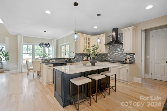 kitchen featuring decorative backsplash, wall chimney exhaust hood, crown molding, a center island, and light hardwood / wood-style floors