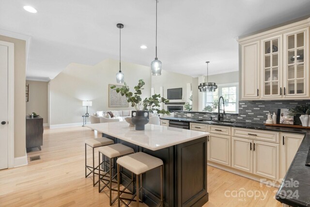 kitchen with cream cabinets, sink, light hardwood / wood-style flooring, decorative light fixtures, and a breakfast bar area