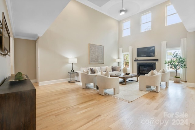 living room featuring crown molding, plenty of natural light, a high ceiling, and light hardwood / wood-style flooring