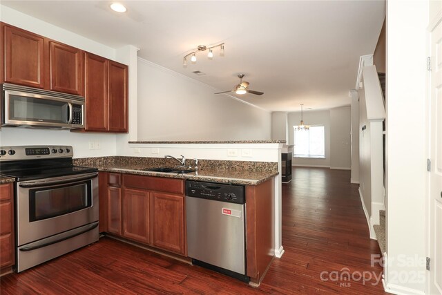 kitchen with appliances with stainless steel finishes, dark wood-type flooring, a sink, dark stone counters, and a peninsula