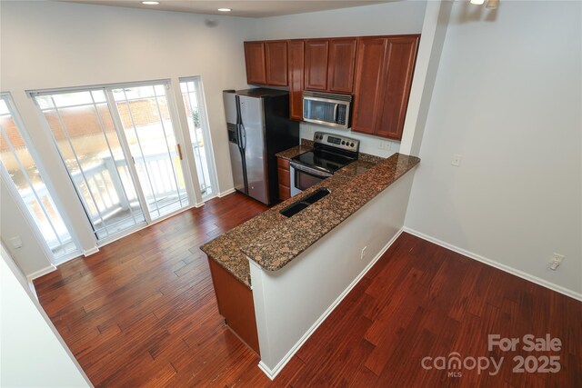 kitchen with brown cabinets, dark stone counters, stainless steel appliances, and dark wood-style flooring