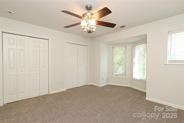 unfurnished bedroom featuring multiple windows, carpet, two closets, and visible vents