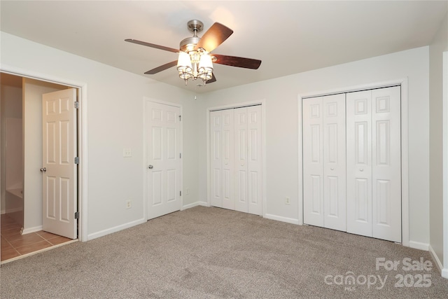unfurnished bedroom with baseboards, two closets, a ceiling fan, and light colored carpet