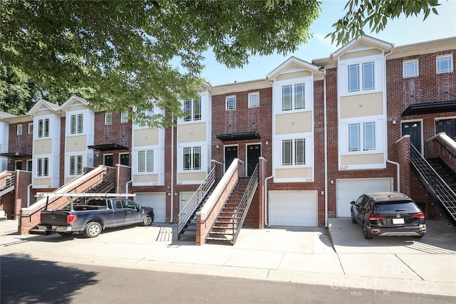 view of property featuring a garage, brick siding, stairs, driveway, and a residential view