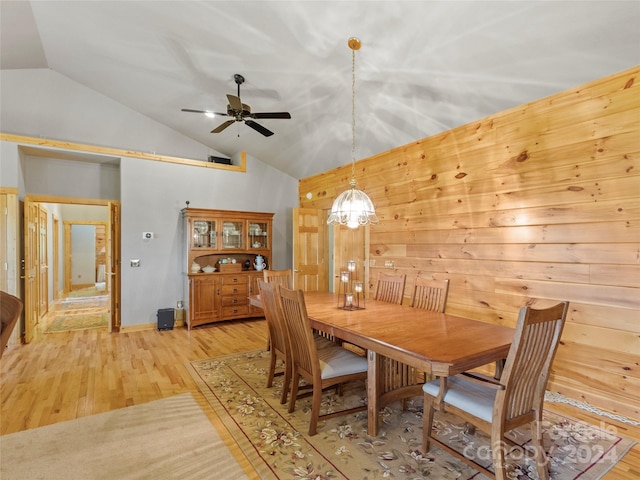 dining room with lofted ceiling, ceiling fan with notable chandelier, wooden walls, and light hardwood / wood-style floors