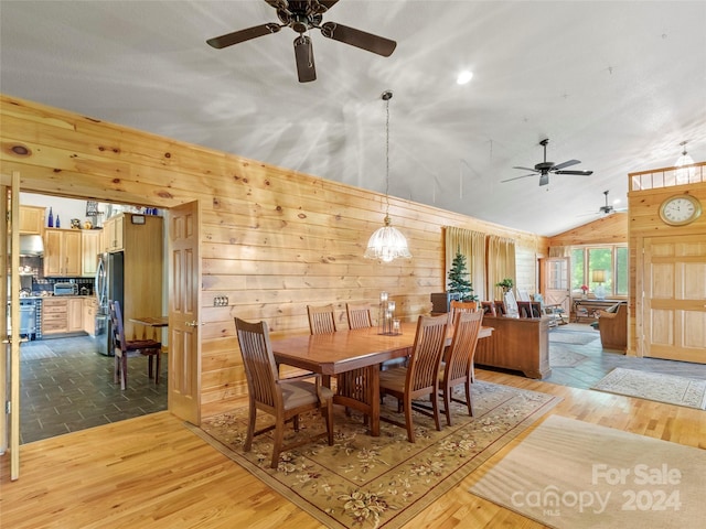 dining room featuring lofted ceiling, an inviting chandelier, wooden walls, and light hardwood / wood-style flooring