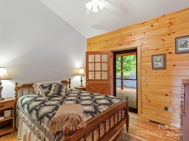 bedroom featuring ceiling fan, access to exterior, vaulted ceiling, wooden walls, and light hardwood / wood-style flooring