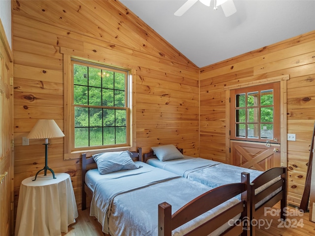 bedroom featuring ceiling fan, wood walls, light hardwood / wood-style flooring, and lofted ceiling