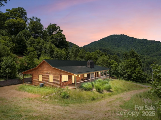 exterior space featuring driveway, a view of trees, a chimney, metal roof, and a mountain view