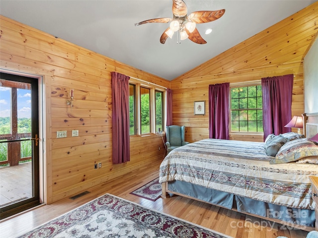 bedroom with lofted ceiling, hardwood / wood-style flooring, wooden walls, and visible vents