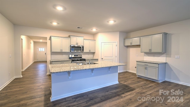 kitchen with gray cabinetry, light stone counters, stainless steel appliances, and dark hardwood / wood-style floors