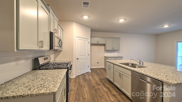 kitchen featuring appliances with stainless steel finishes, light stone counters, sink, dark hardwood / wood-style floors, and an island with sink