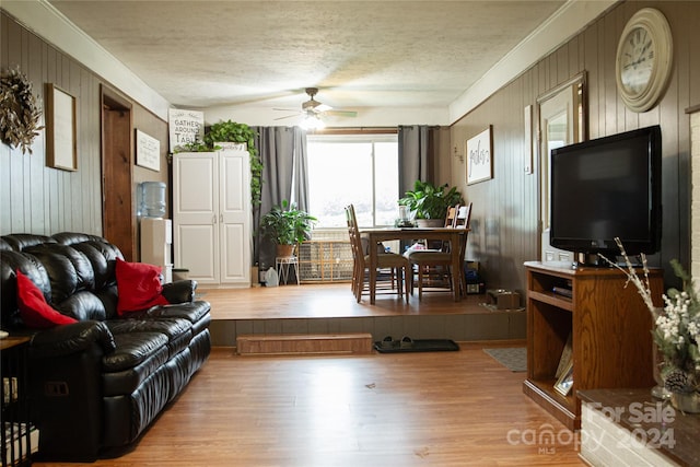 living room with a textured ceiling, light wood-type flooring, and wooden walls