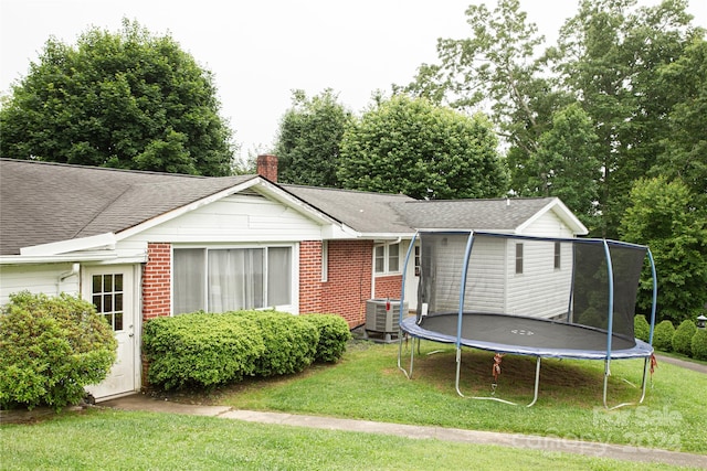 back of property featuring cooling unit, a yard, and a trampoline