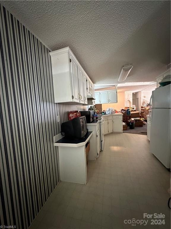 kitchen featuring a textured ceiling, kitchen peninsula, white cabinetry, and white appliances