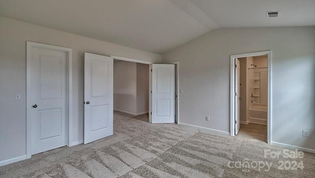 unfurnished bedroom with vaulted ceiling, light colored carpet, and ensuite bath