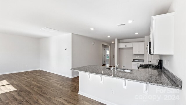 kitchen with kitchen peninsula, stainless steel range, a breakfast bar, sink, and white cabinets