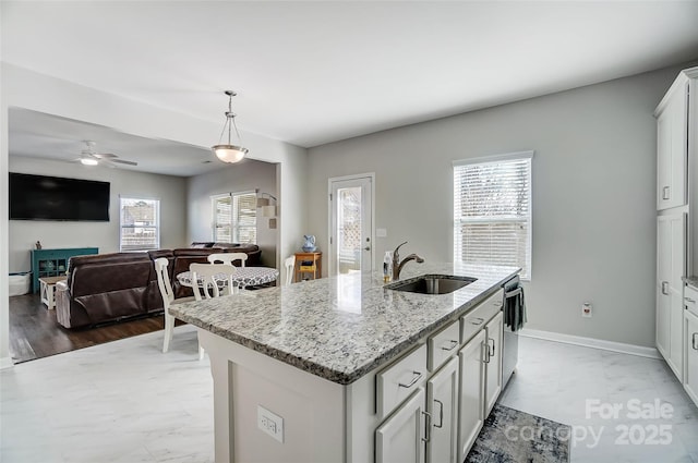 kitchen featuring ceiling fan, sink, light stone counters, an island with sink, and decorative light fixtures