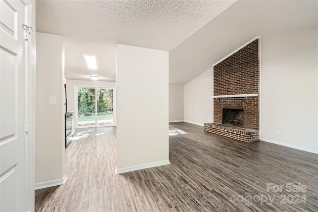 unfurnished living room with a textured ceiling, dark hardwood / wood-style floors, a brick fireplace, and lofted ceiling