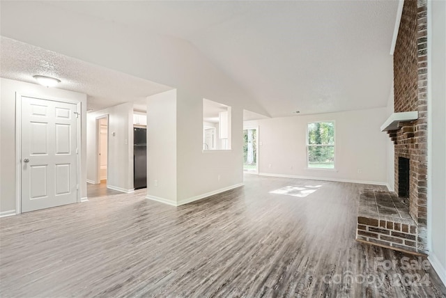 unfurnished living room featuring a textured ceiling, hardwood / wood-style floors, lofted ceiling, and a brick fireplace