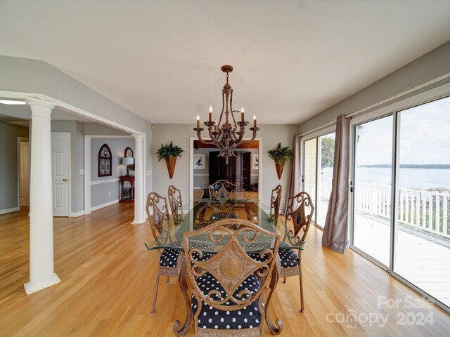 dining space featuring decorative columns, light hardwood / wood-style floors, a chandelier, and a water view