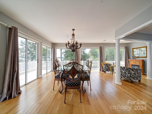 dining area with decorative columns, a tile fireplace, light hardwood / wood-style flooring, and a notable chandelier