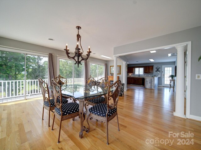 dining area featuring light wood-type flooring, a notable chandelier, and decorative columns