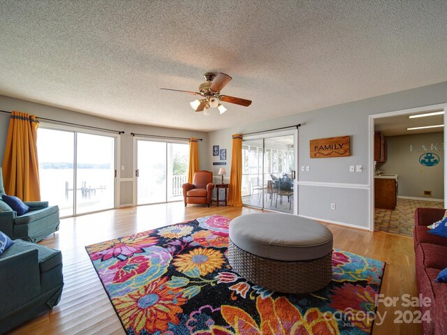 living room with a water view, ceiling fan, a textured ceiling, and light hardwood / wood-style floors