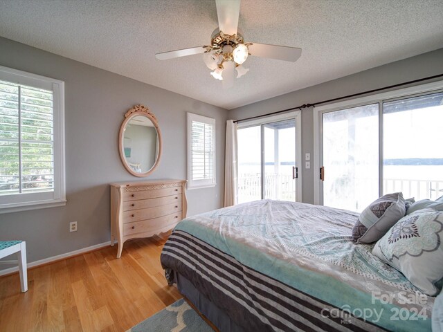 bedroom featuring a textured ceiling, ceiling fan, a water view, and access to outside