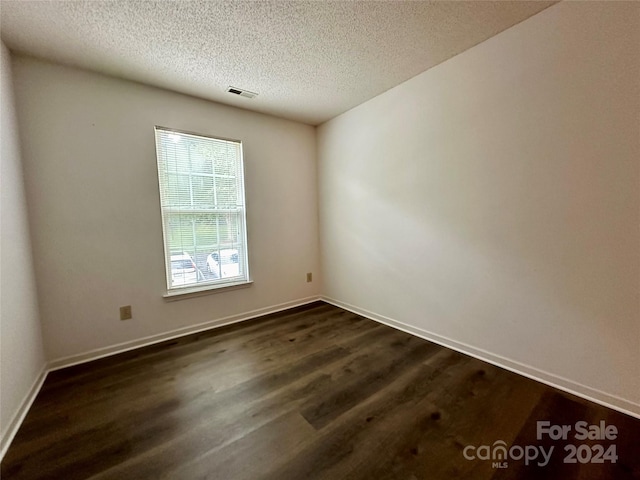 empty room with dark hardwood / wood-style flooring and a textured ceiling